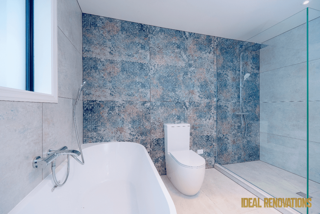 Modern bathroom with a white tub, toilet, shower area, and blue textured tiles, project done by Ideal Renovations